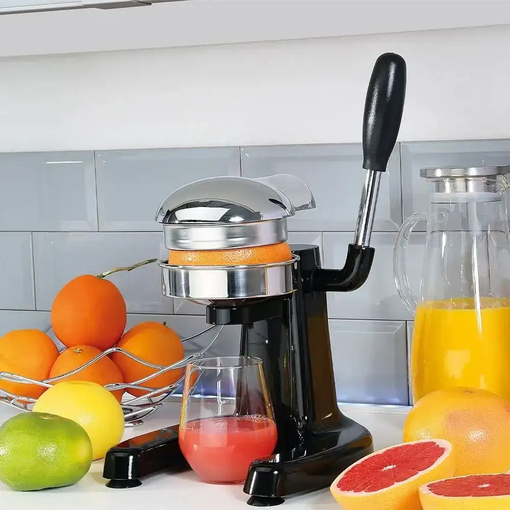 Manual juicer with oranges and a glass of juice on a kitchen counter.
