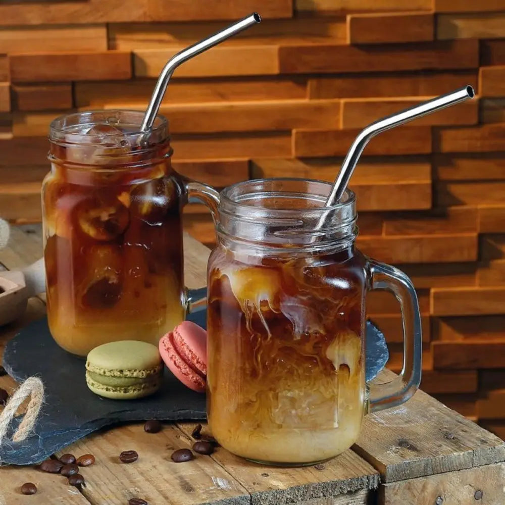 Two glass mugs with iced coffee and straws on a wooden surface with a wooden background.