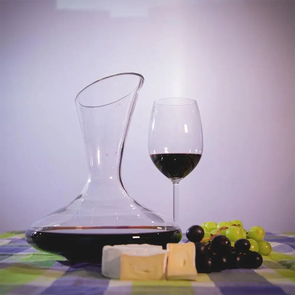 Wine decanter, glass of red wine, grapes, and cheese on a checkered tablecloth.