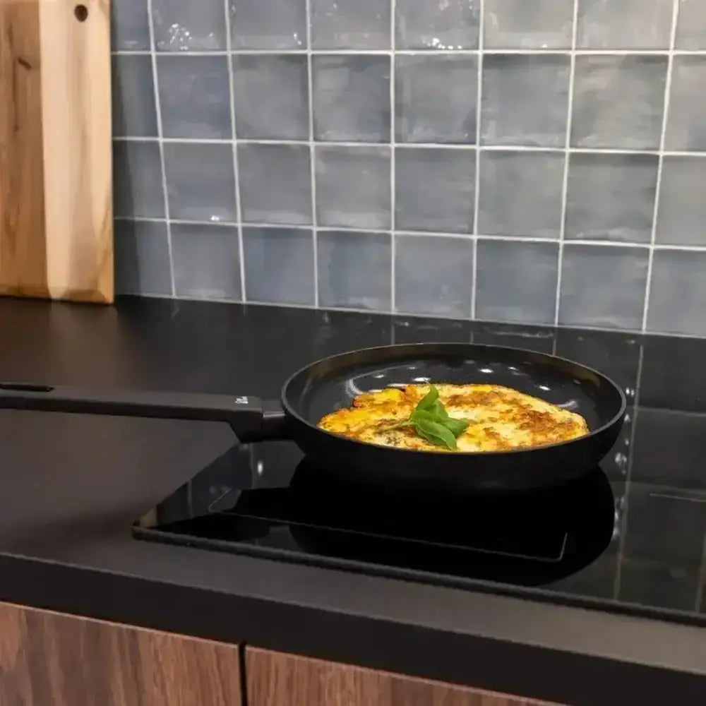 Cosy and trendy full black ceramic non-stick frying pan 24cm with long handle containing golden omelette and basil leaves