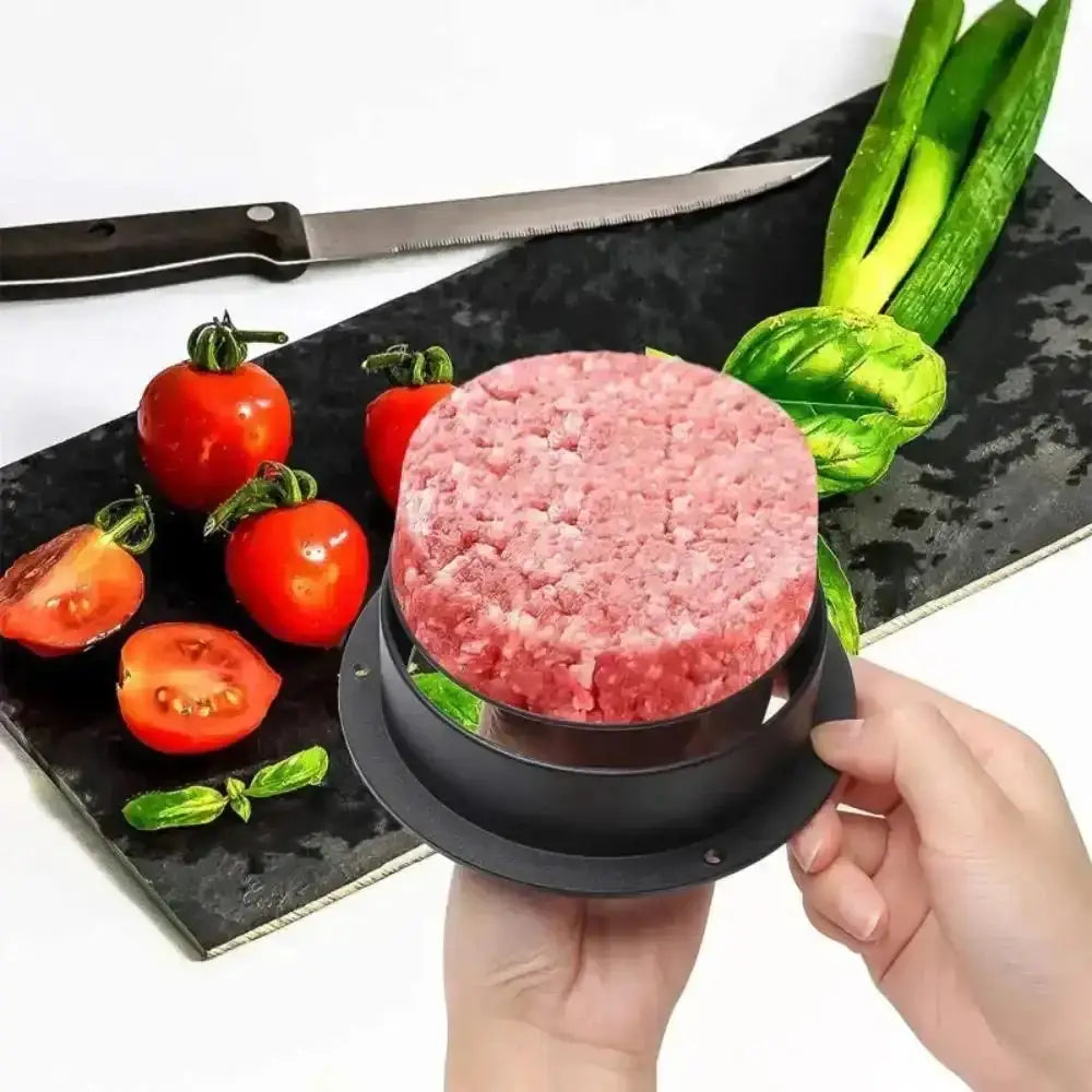 Hamburger patty maker with a patty on a black surface with tomatoes and basil