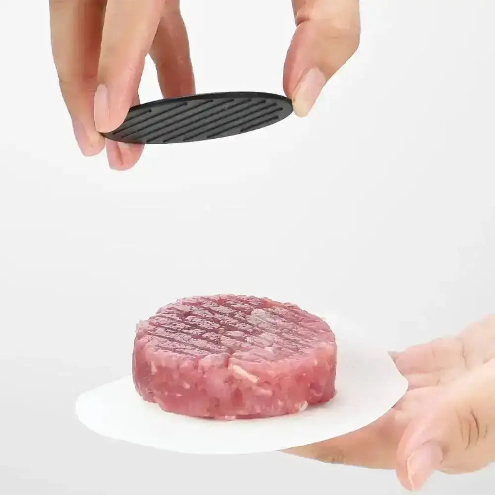 Person using a black grill tool on a raw hamburger patty.