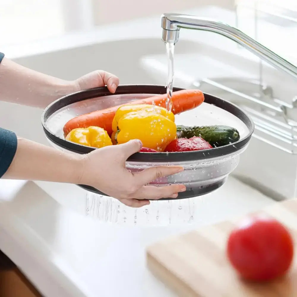 Person washing vegetables in a colander under running water in a kitchen sink.