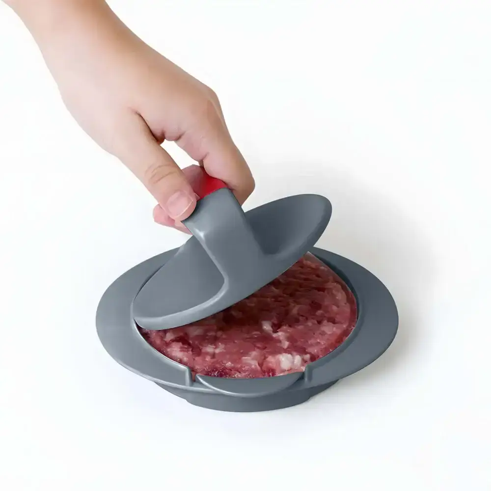 Hand using a gray burger press on ground meat on a white background