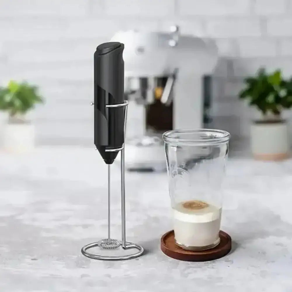 Handheld milk frother with a glass of frothed milk on a kitchen counter.