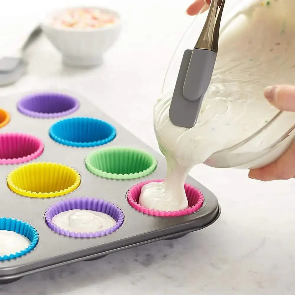 Person filling colorful silicone cupcake liners with batter using a spatula.