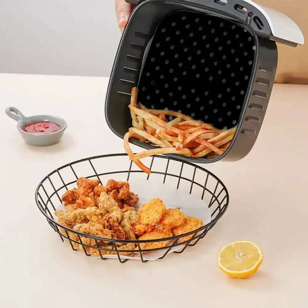 Black air fryer basket with fried food on a white surface with a lemon and small bowl.