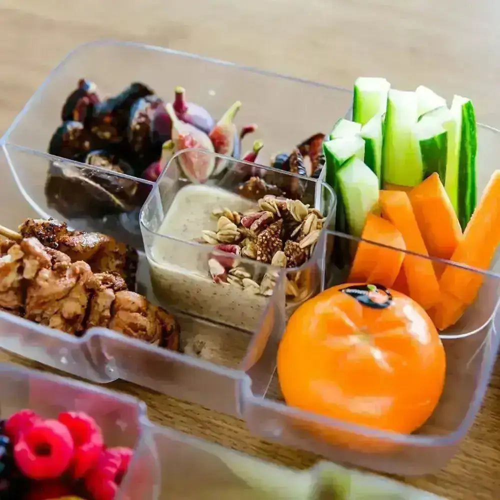 Clear lunchbox with fresh vegetables, fruit, grilled chicken, granola, and dip from Cookin Stores.