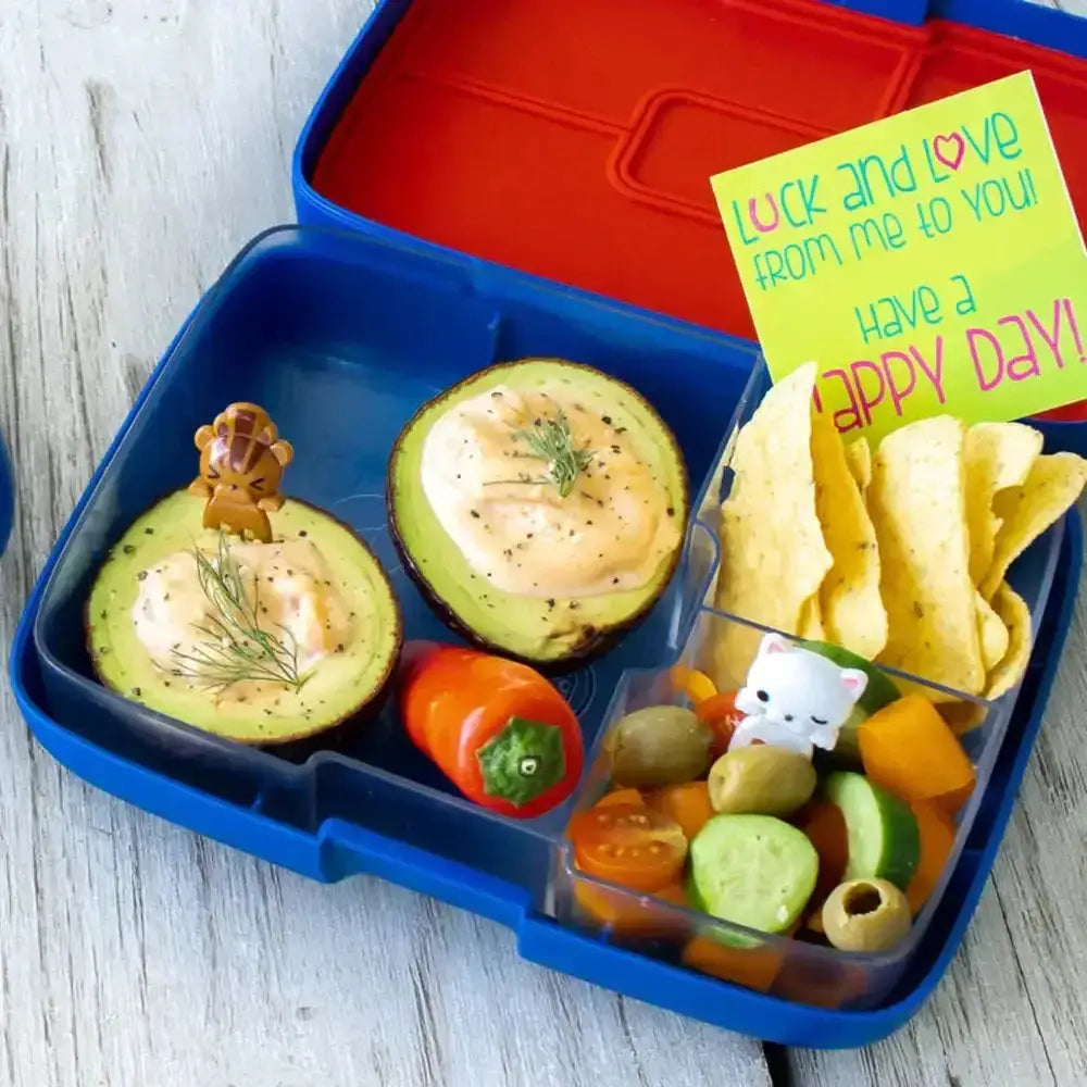 Blue three-compartment lunchbox with avocado halves, chips, fresh vegetables, and a cheerful note from Cookin Stores.