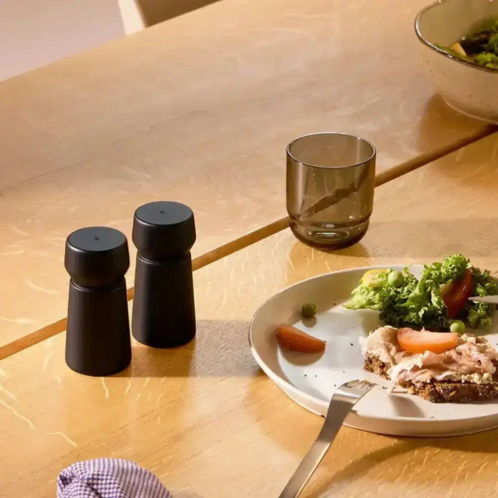 Black beech wood salt and pepper grinder set on dining table with food and glass