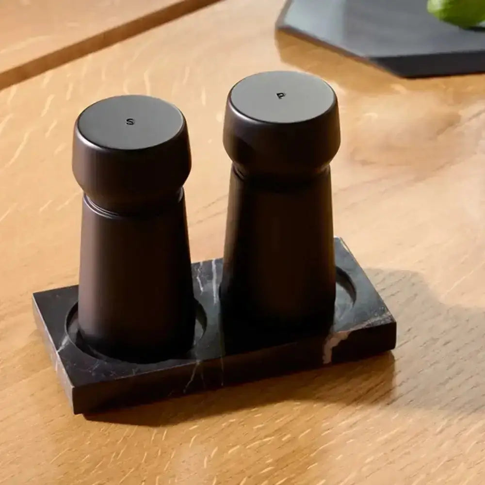 Black wooden salt and pepper grinders set on a marble tray on a wooden table