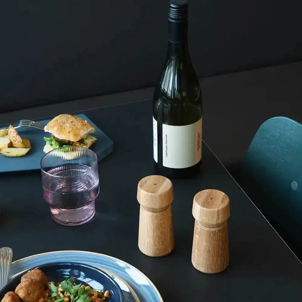 Pair of oak wood salt and pepper grinders on a modern dining table with food and drink
