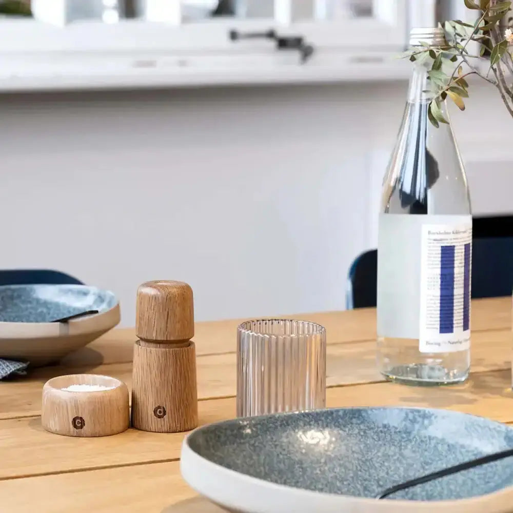 Table setting with wooden salt and pepper shakers, glass, and water bottle on a wooden table.
