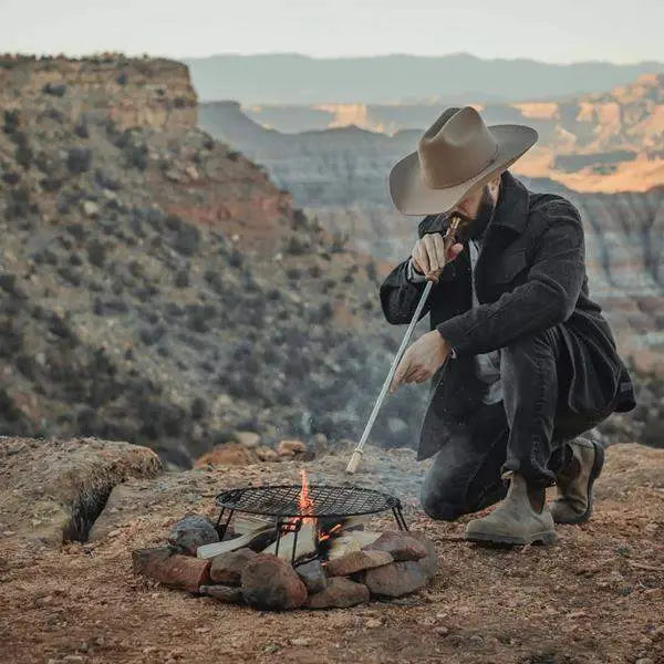 Man using brass fire blower outdoors at campfire, Cookin Stores premium kitchenware