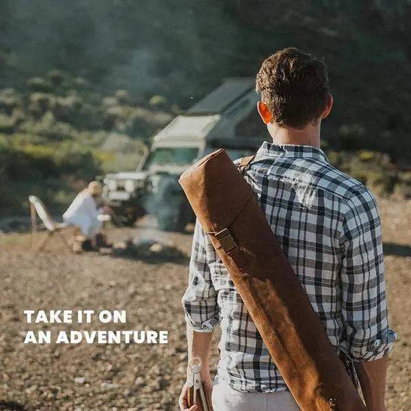 Man carrying brown leather jack sack outdoors near SUV and campfire, adventure gear from Cookin Stores