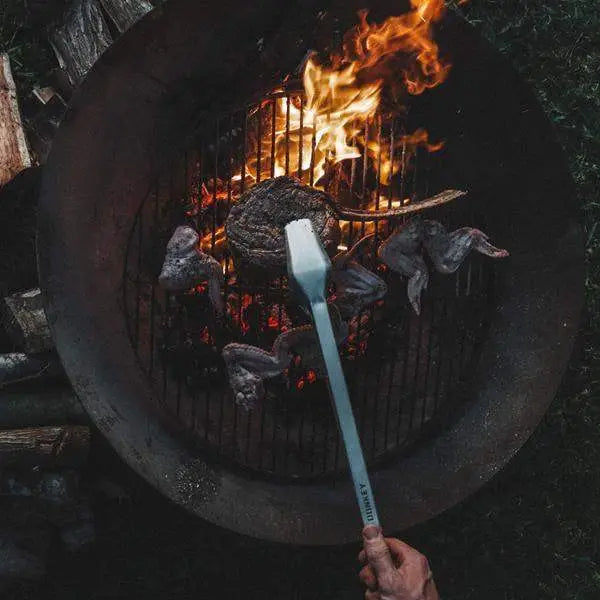 Barbecue grill with steak and chicken wings, metal tong turning food, outdoor cooking tool