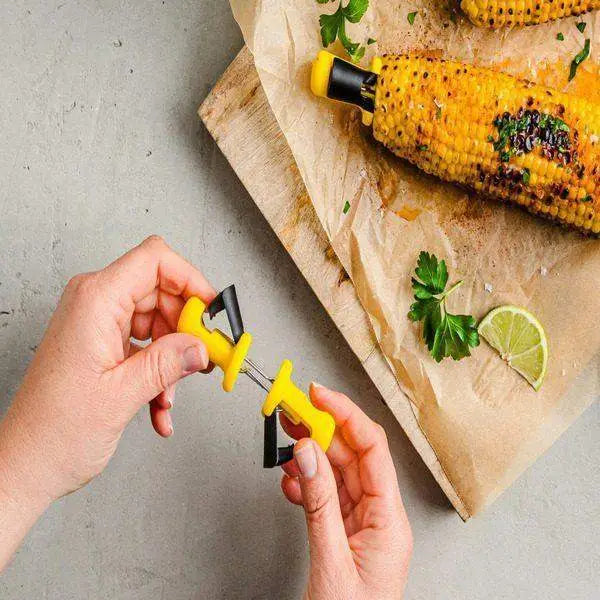 Hands assembling Dreamfarm Anchor Corn Lockorns holders beside grilled corn on parchment, Cookin Stores kitchenware