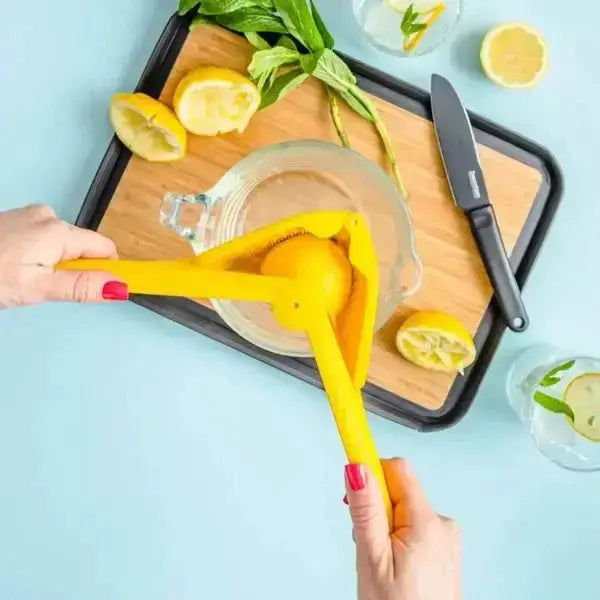 Yellow lemon juicer pressing fresh lemon on cutting board, kitchen knife, and glass jug, Cookin Stores kitchenware