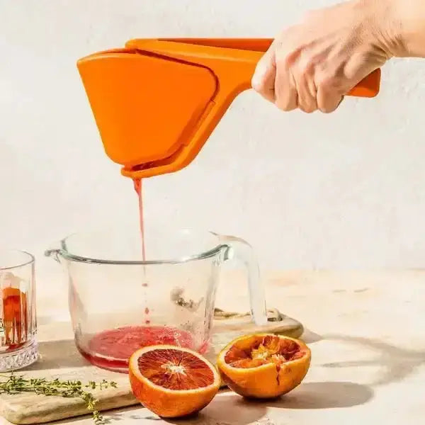 Hand using orange Dreamfarm Fluicer lemon squeezer for blood orange juice in glass jug, Cookin Stores