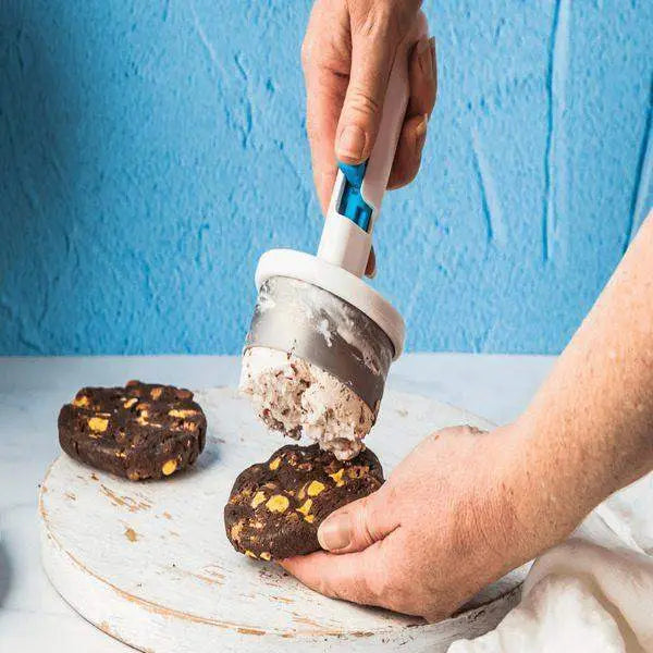 Hand using Dreamfarm Icepo ice cream scoop to prepare ice cream cookie sandwiches on a white board