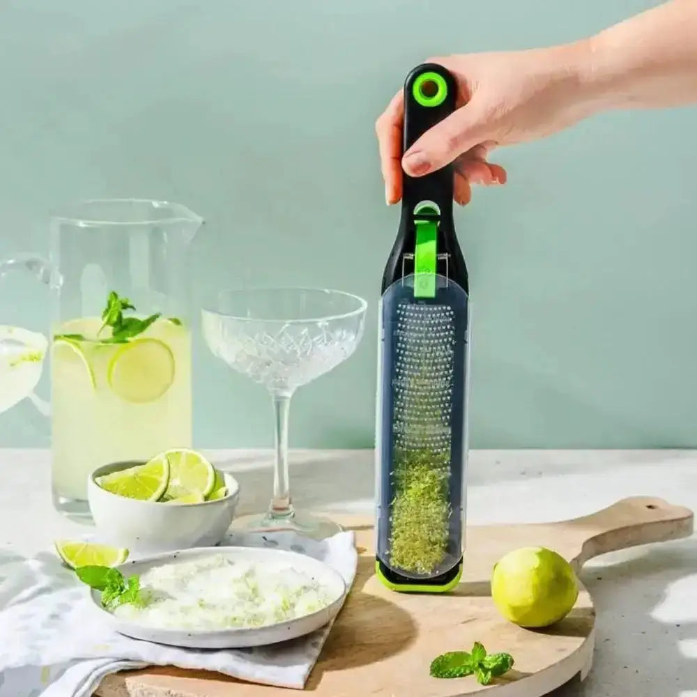 Hand holding a bottle with a lime using a grater, with a drink setup in the background.