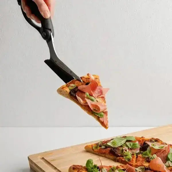 Black pizza scissors cutting and serving a slice of fresh pizza on a wooden board