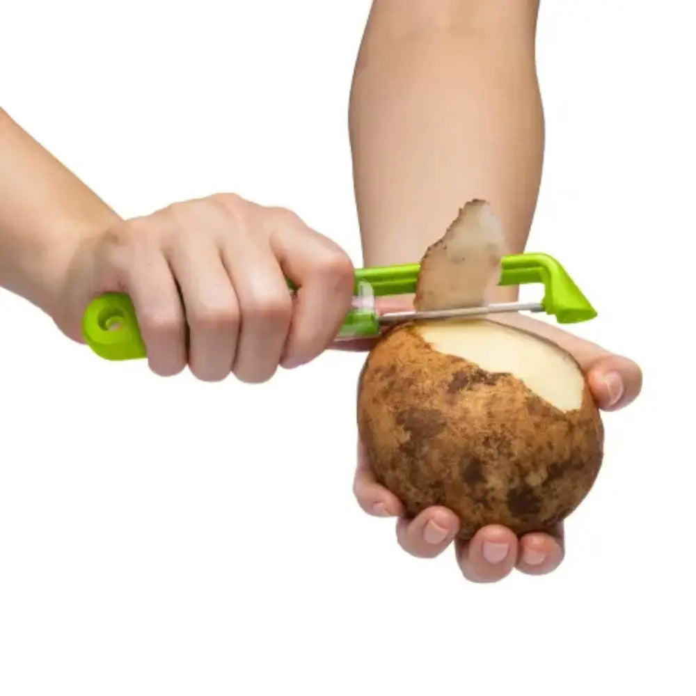 Person peeling a potato with a green peeler on a white background