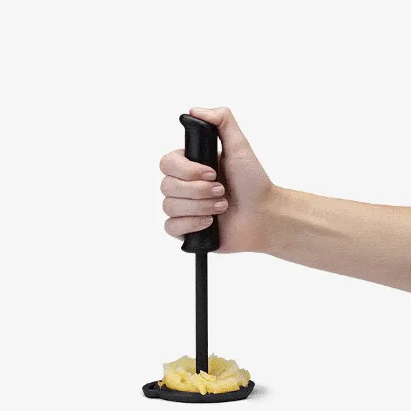 Hand using a black potato masher to mash potatoes on a white background