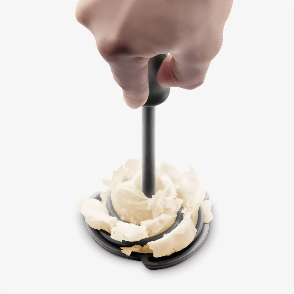 Hand using a kitchen tool to shape mashed potatoes on a white background