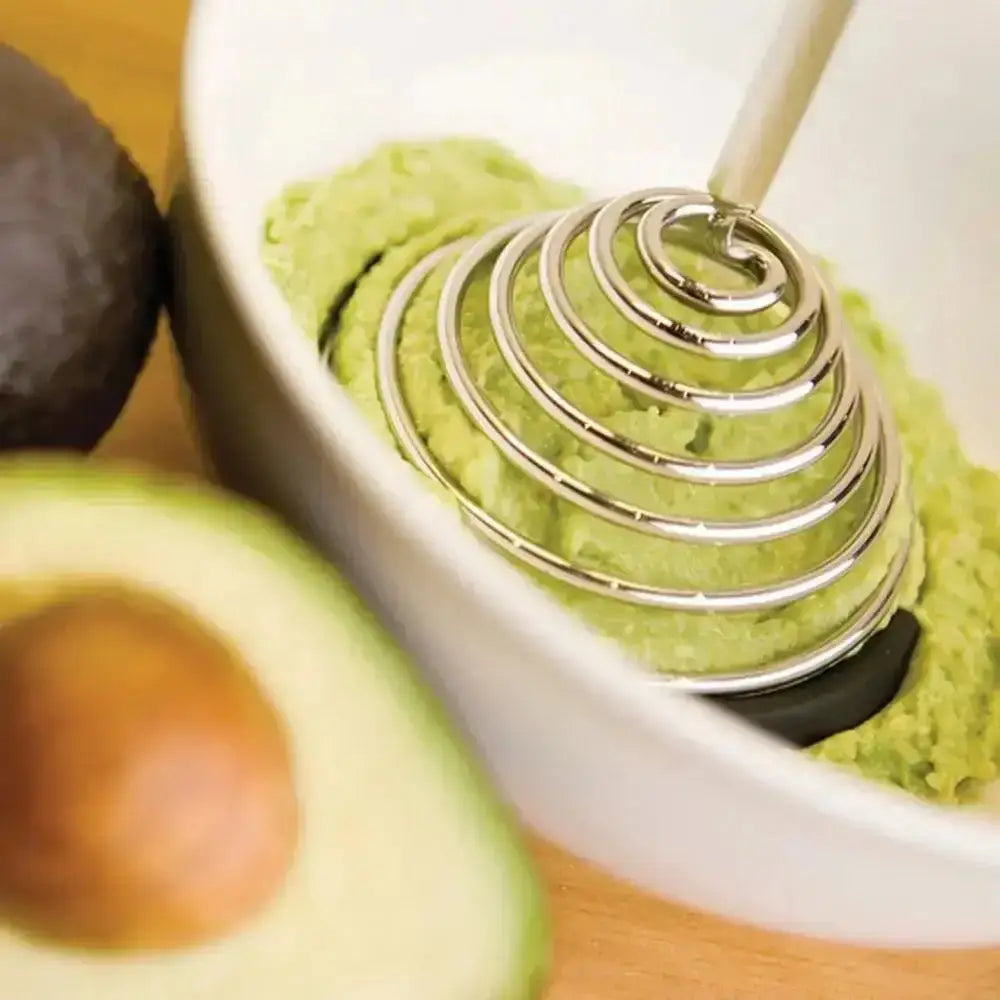 Dreamfarm Smood masher mashing avocado in a white bowl, avocado halves in foreground, Cookin Stores kitchenware.