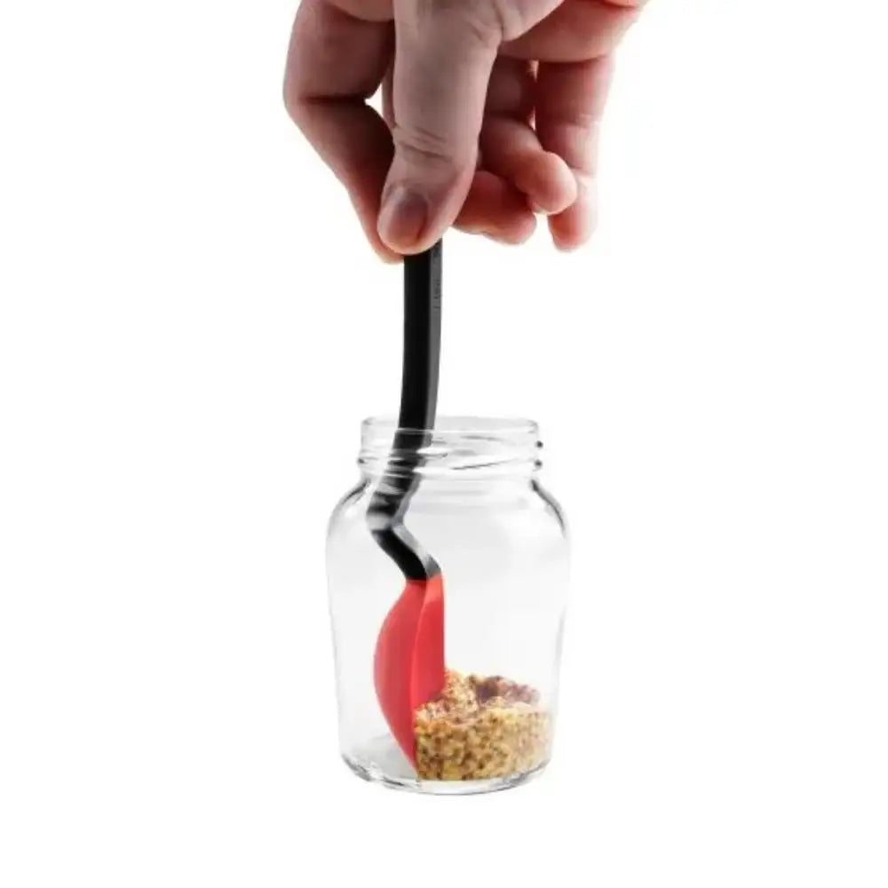 Hand holding a black and red spoon over a jar of spices on a white background