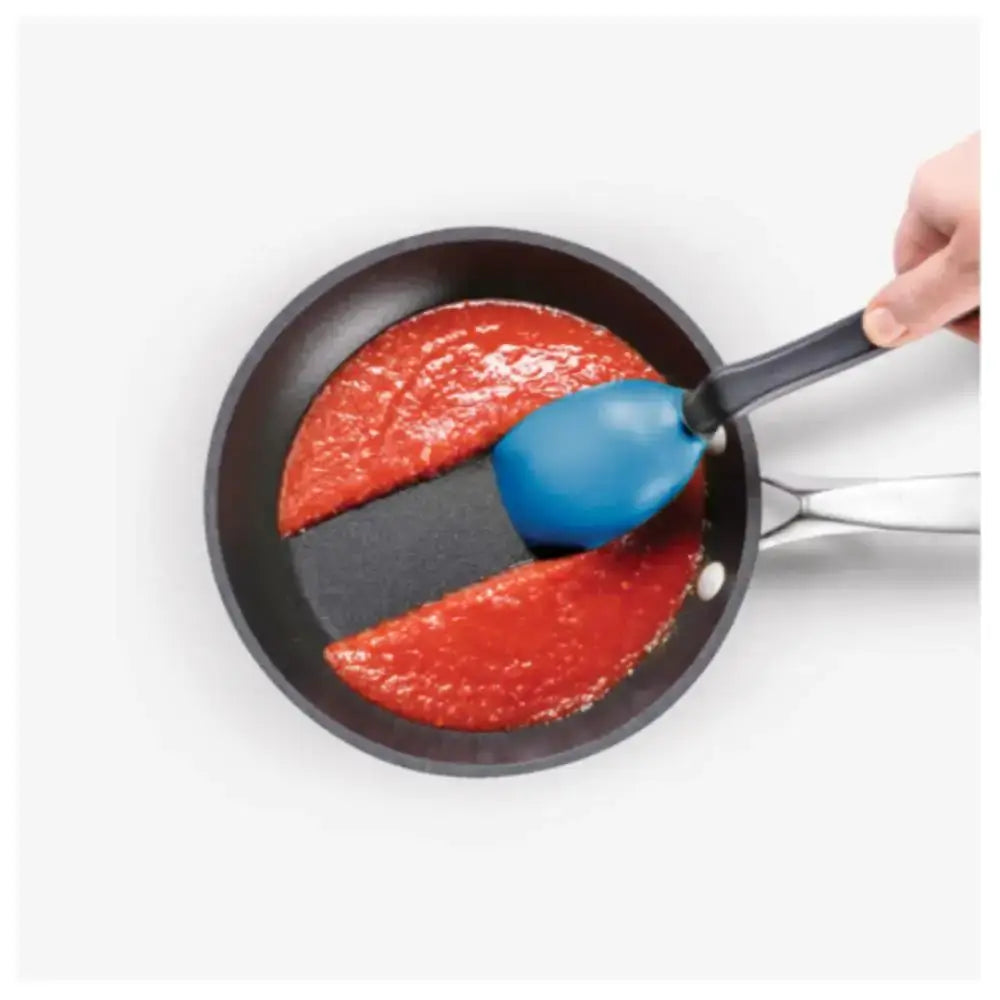 Nonstick frying pan with tomato sauce being stirred by a blue silicone spatula