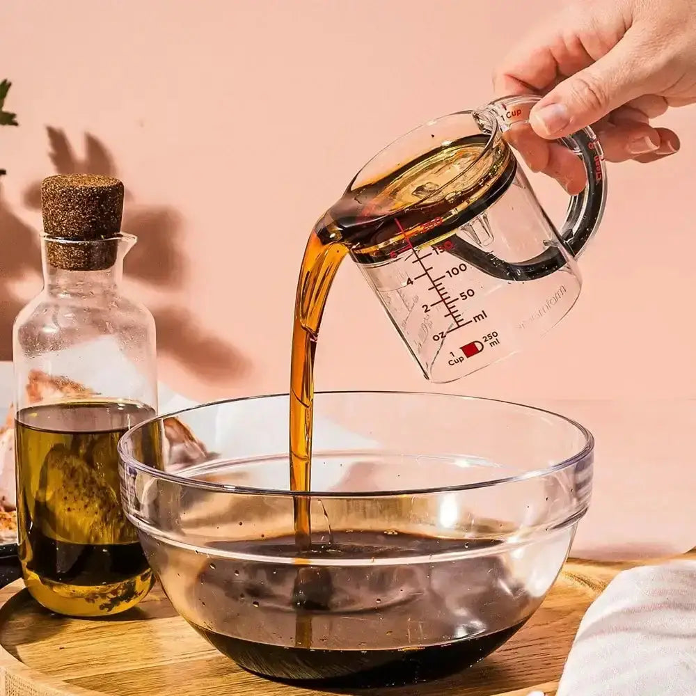 Person pouring liquid from a measuring cup into a glass bowl with a pink background