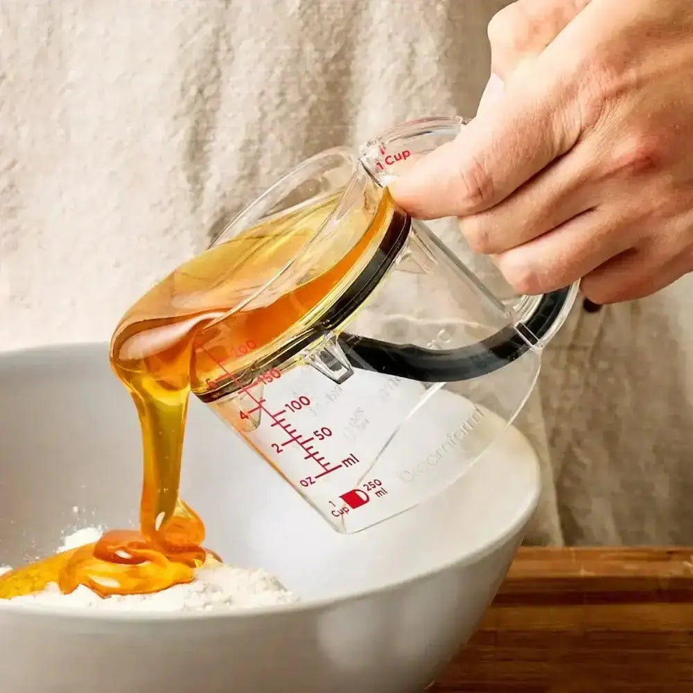 Hand pouring honey from a measuring cup into a bowl