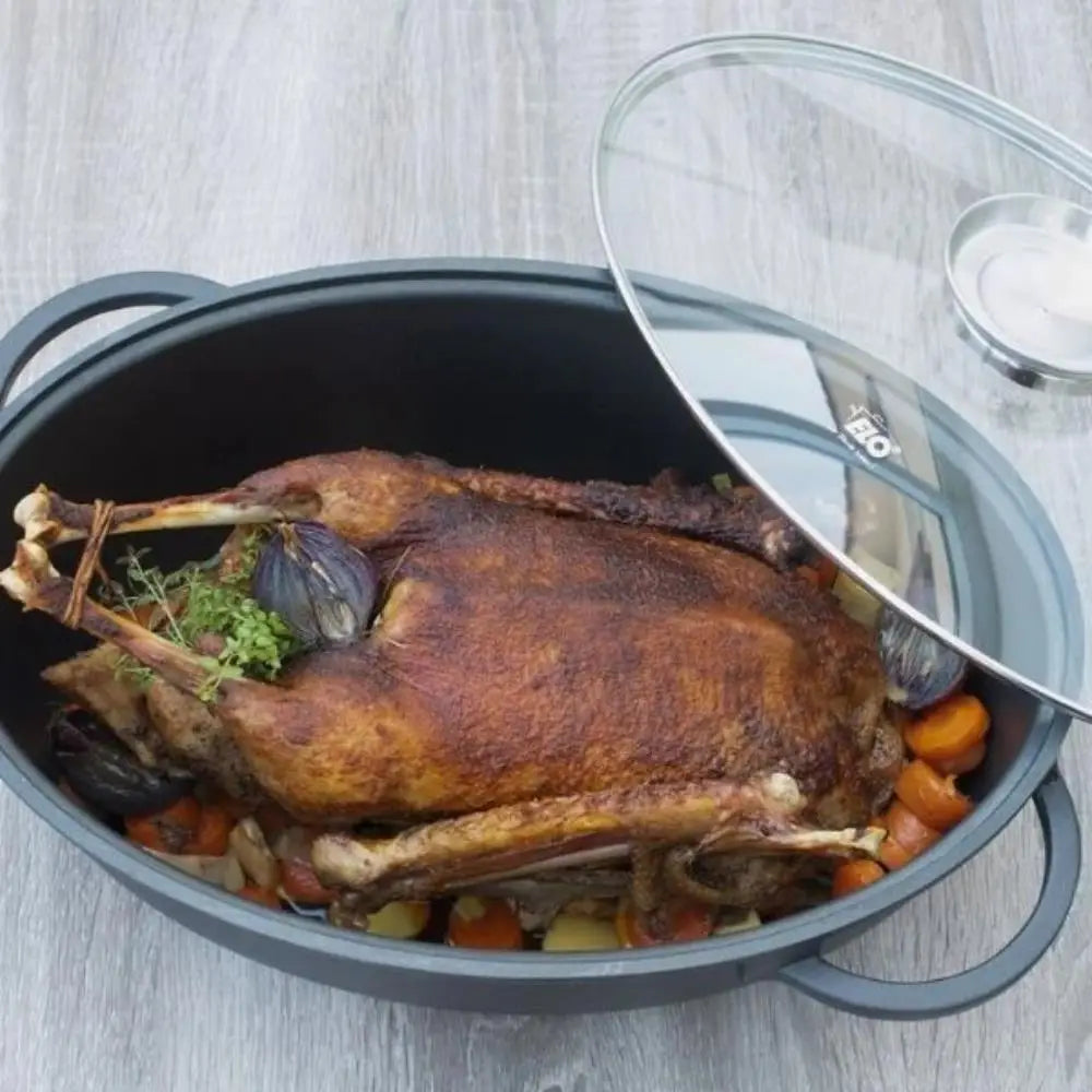 Roasted duck with vegetables in a black roasting pan on a light wooden surface