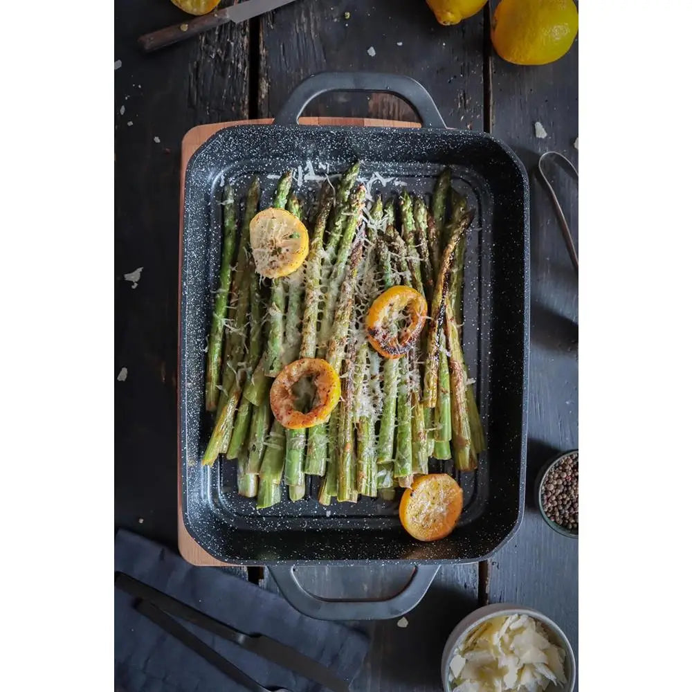 Roasted asparagus with lemon slices on a black speckled baking tray.
