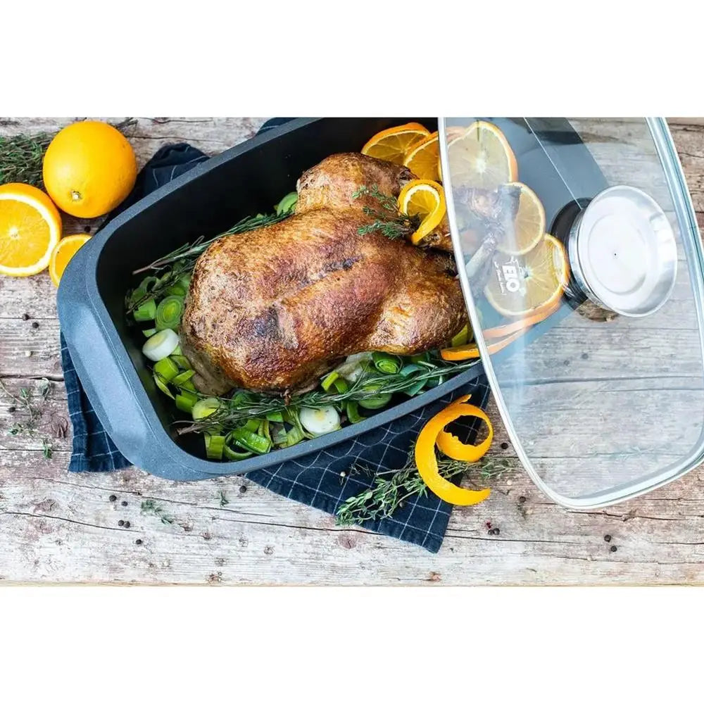 Roasted turkey with herbs and citrus in a roasting pan on a wooden surface.