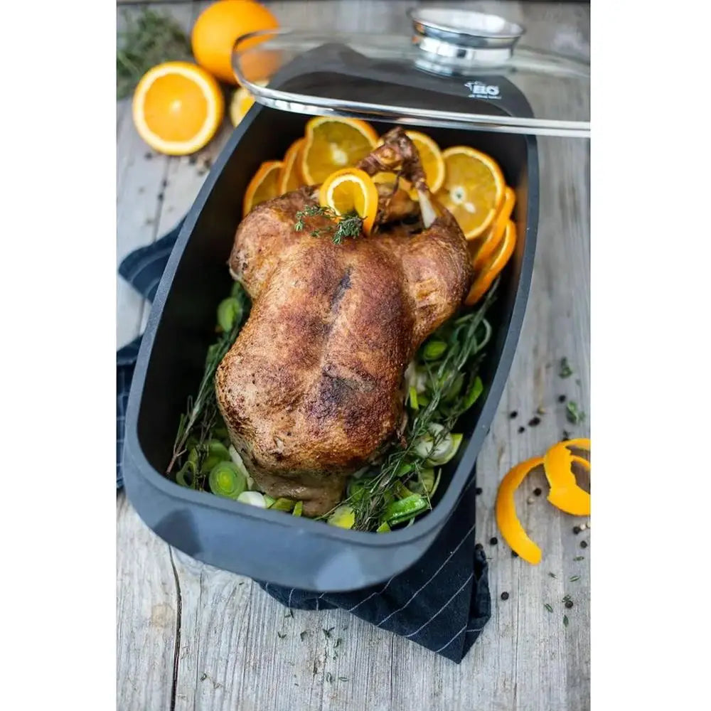Roasted turkey with oranges and herbs in a roasting pan on a wooden surface.