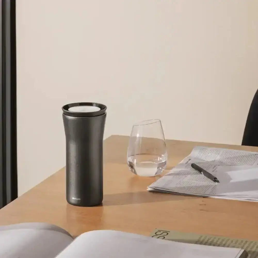 Eva Solo City To Go Cup 350ml black travel mug on office desk with glass, papers, and pen at Cookin Stores
