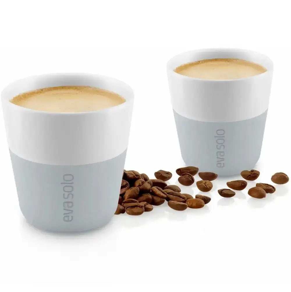 Two white and gray coffee cups with espresso and scattered coffee beans on a white background