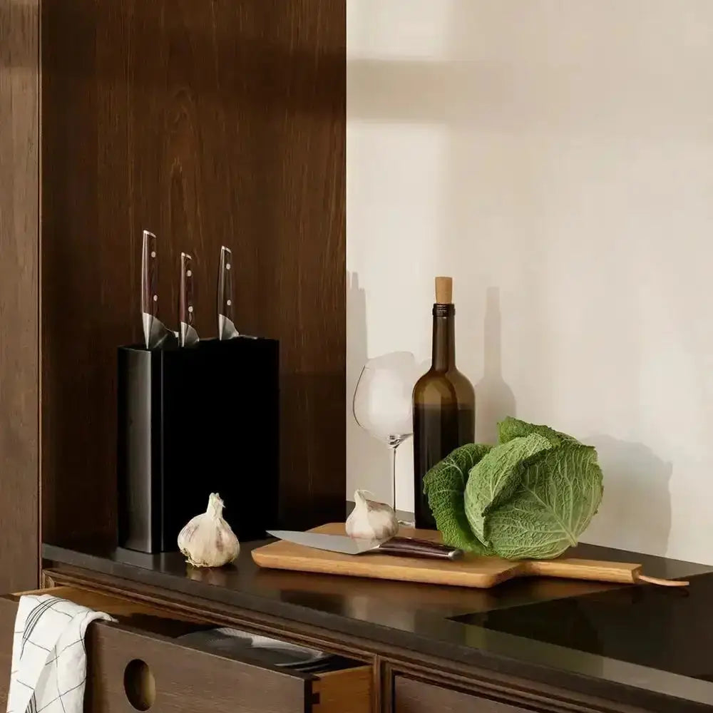 Modern black knife stand with knives on kitchen counter, cutting board, garlic, cabbage, wine bottle at Cookin Stores
