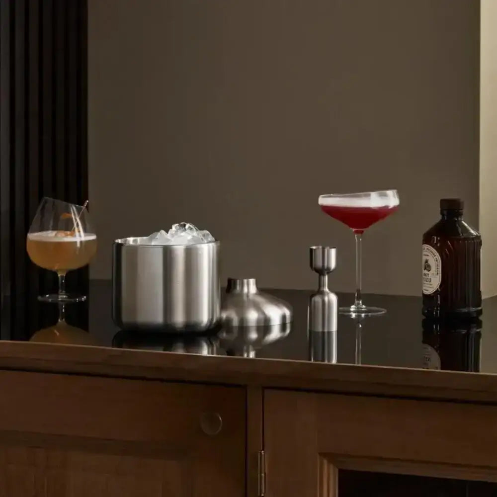 Stainless steel cocktail jigger, ice bucket, and drinks on dark countertop at Cookin Stores