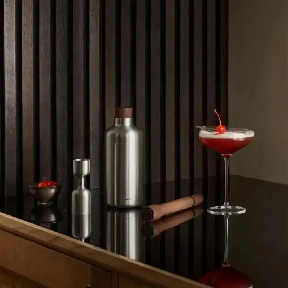 Cocktail with a cherry garnish on a bar counter with bar tools.