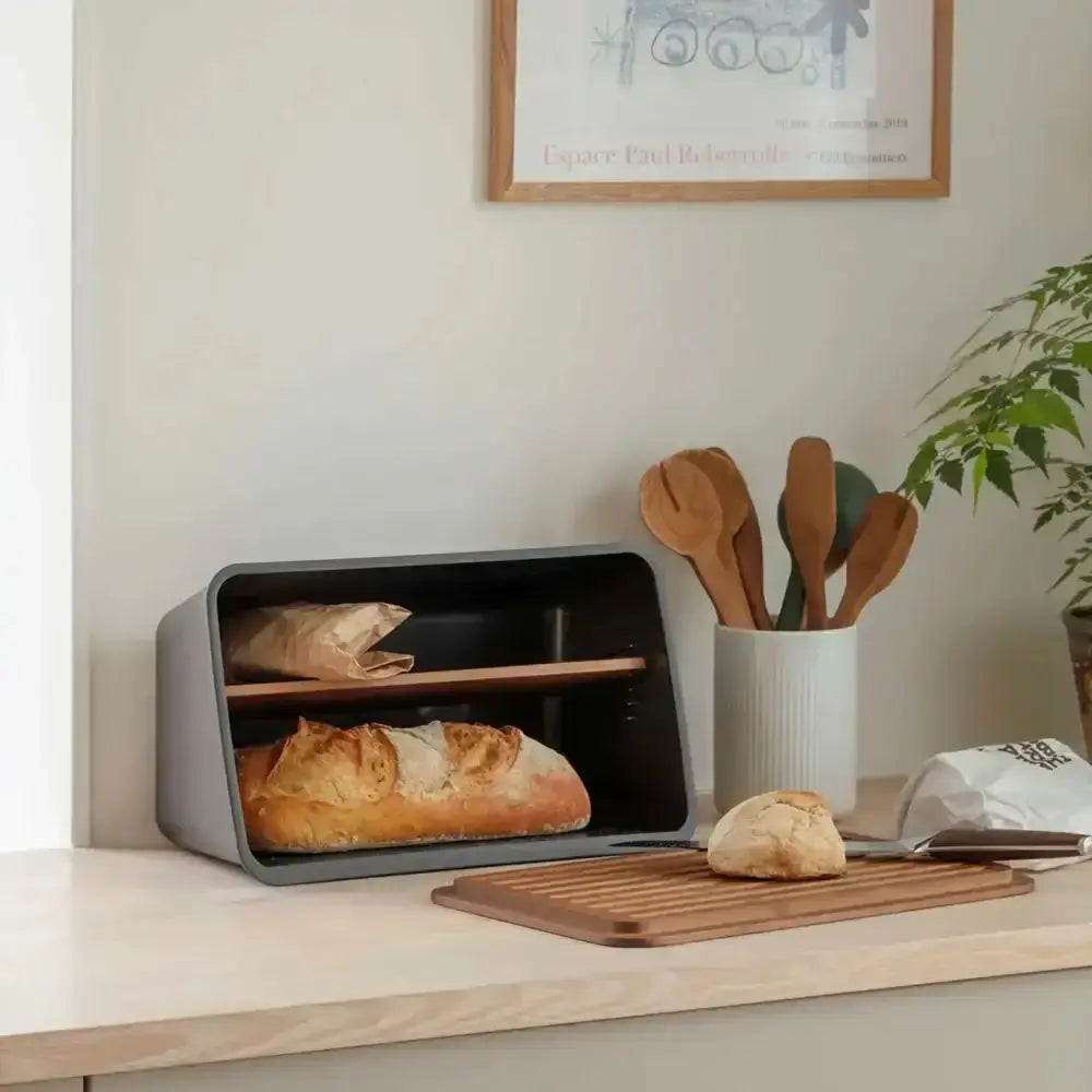 Bread box with bread slices on a wooden shelf with a plant and framed picture in the background.