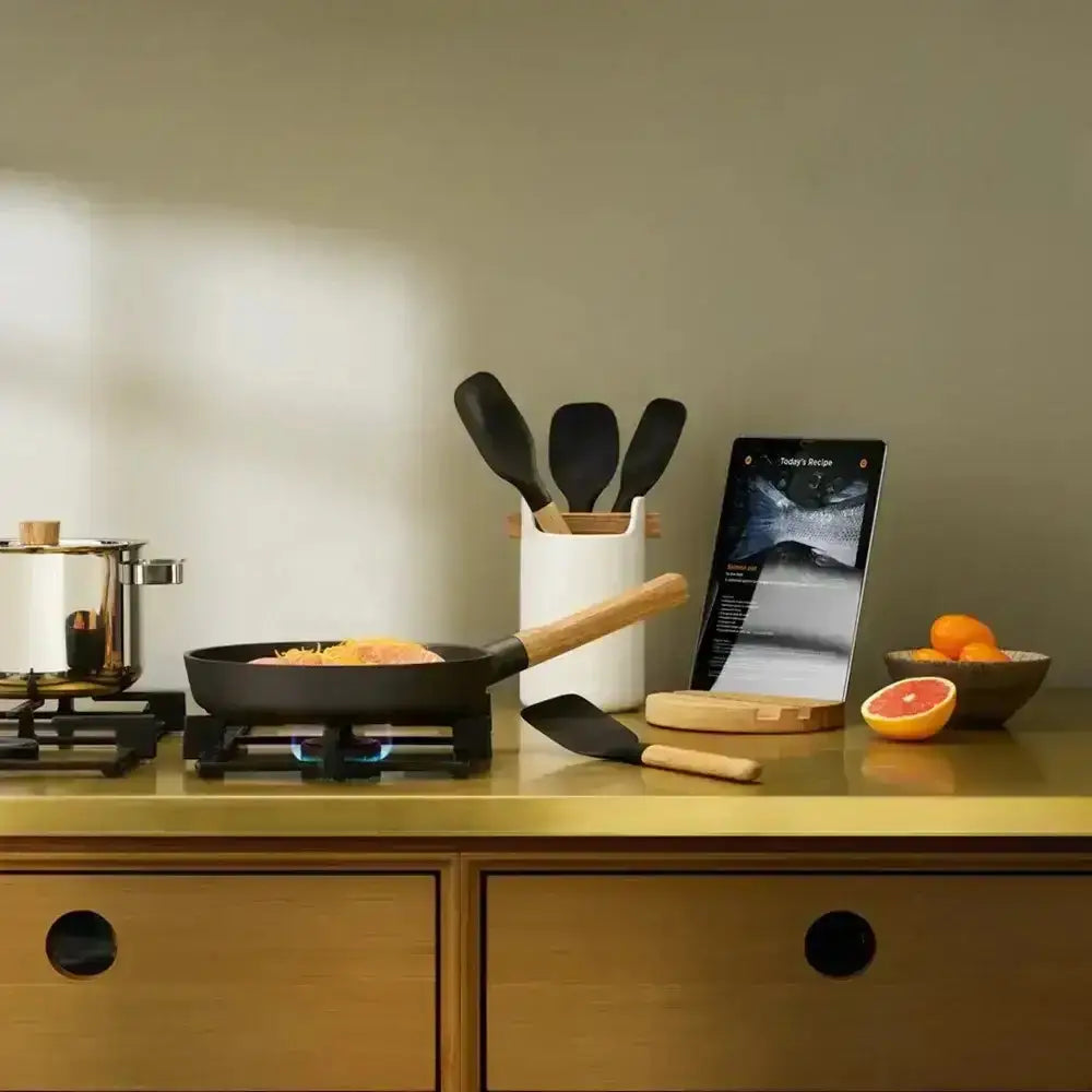 Kitchen counter with cooking pan, utensils, and smartphone displaying a recipe app.