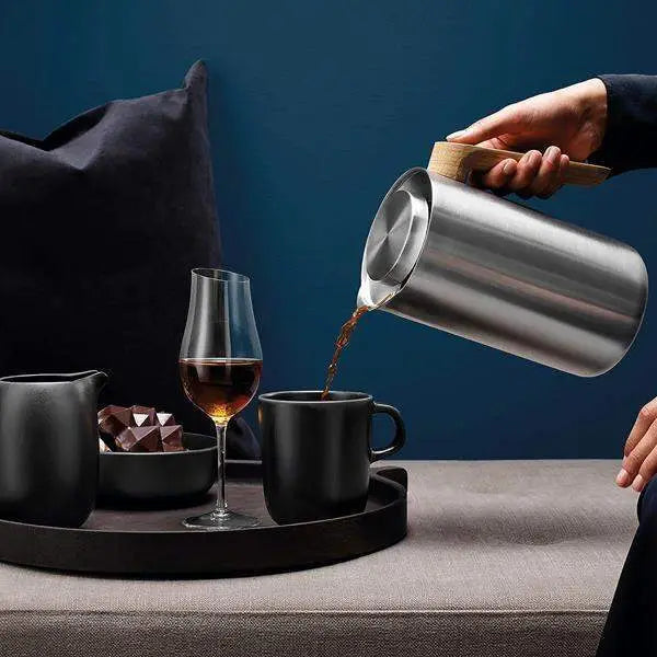 Stainless steel carafe pouring coffee into a black mug on a tray with glassware, Cookin Stores kitchenware