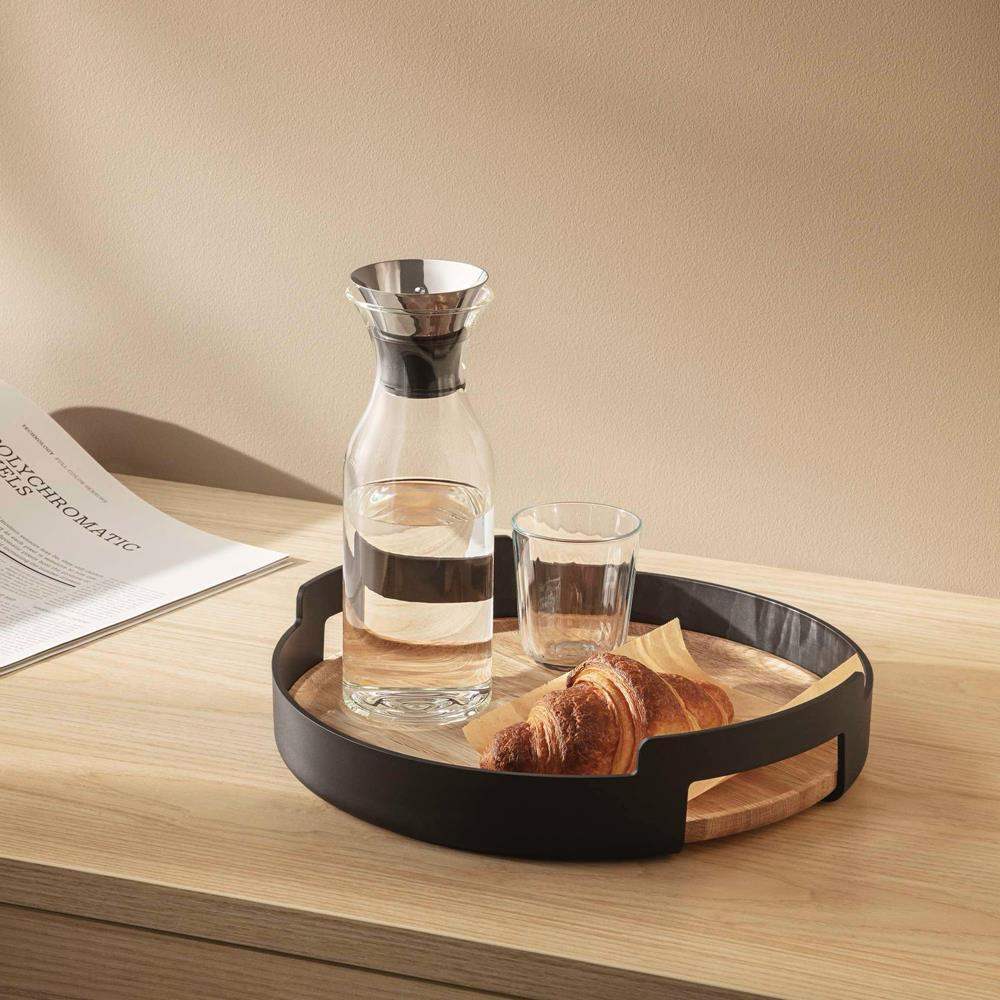 Eva Solo Nordic round oak serving tray with glass carafe, glass, and croissant on tabletop