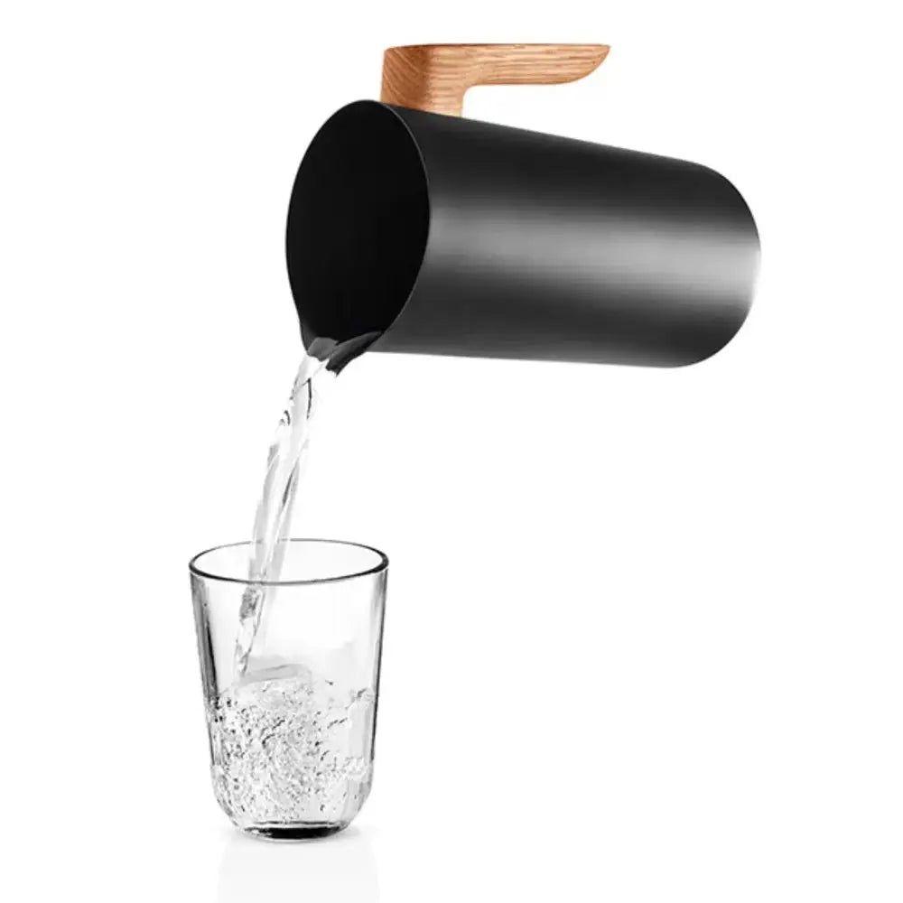 Black pitcher with wooden handle pouring water into a glass on a white background