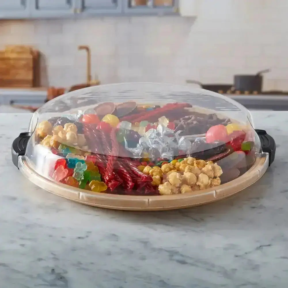 Clear lid on a platter with snacks including popcorn and gummy bears, set on a marble countertop.