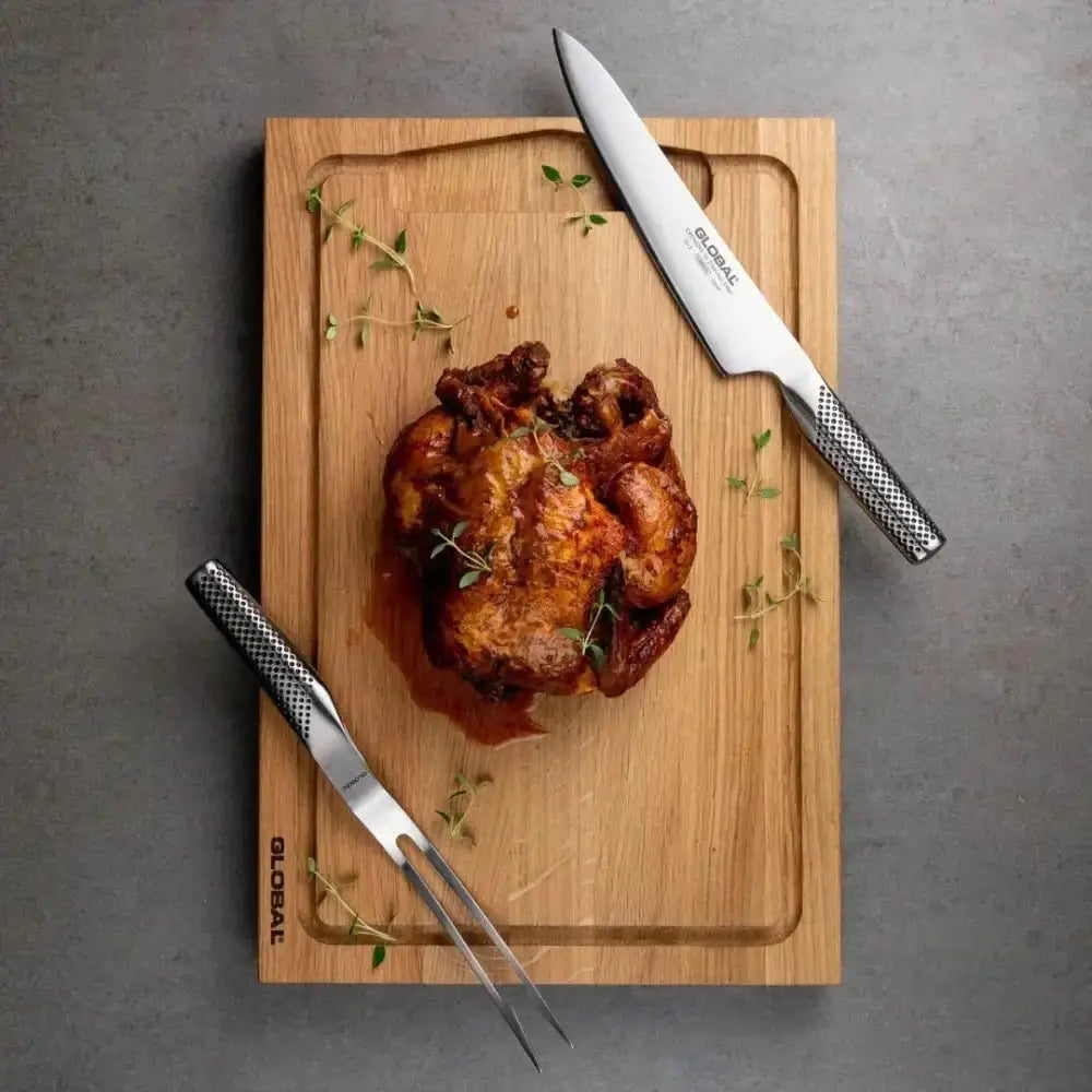 Roasted chicken on a wooden cutting board with two knives on a gray surface